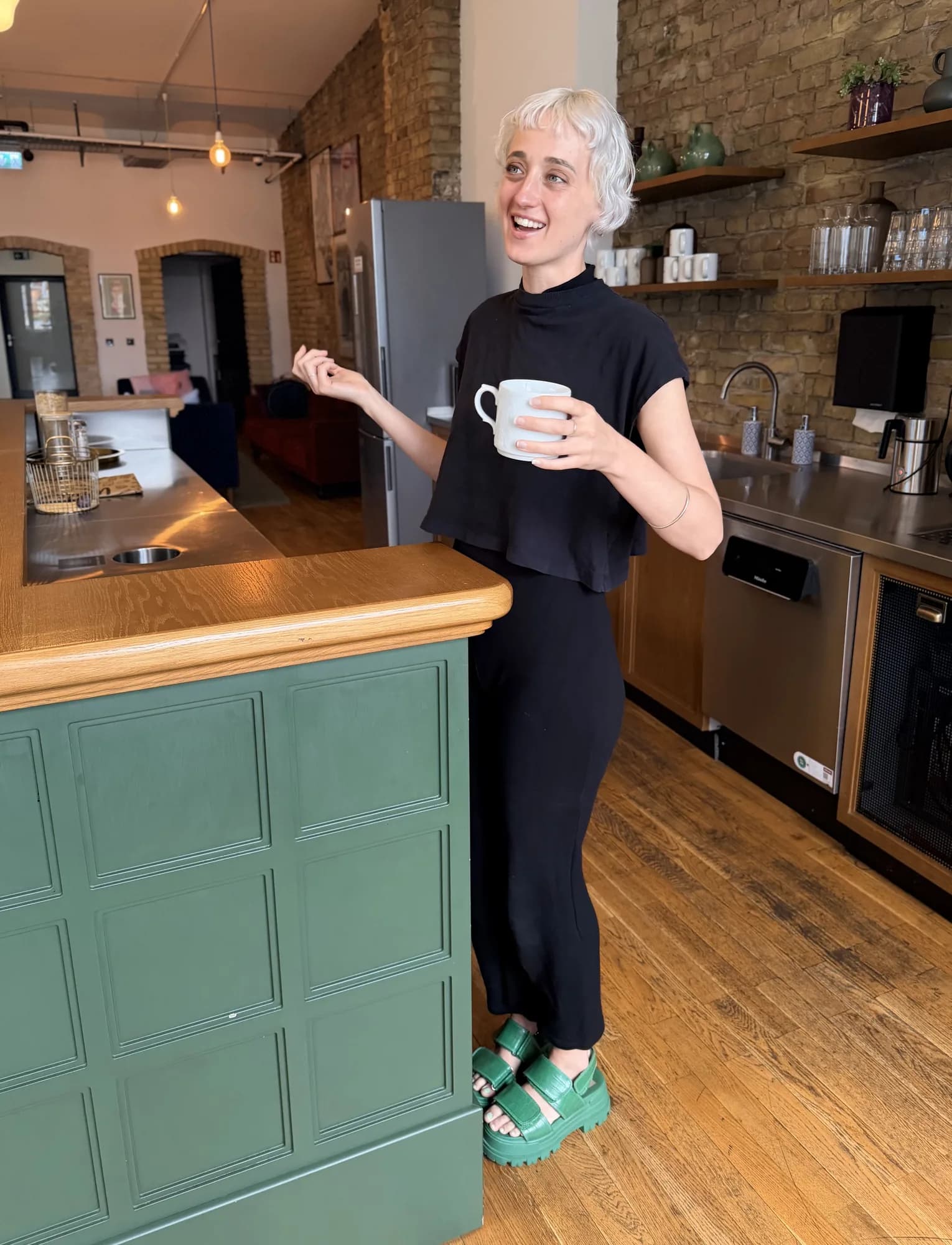 Amber Hoffman lacht in einer Küche und hält eine Tasse Kaffee
